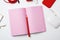 Open pink paper notebook, power bank with cable, red smartphone, headphones, wireless mouse