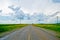 Open road beneath a cloudy sky between sunflower fields