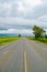 Open road beneath a cloudy sky between sunflower fields