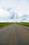 Open road beneath a cloudy sky between sunflower fields