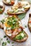 Open sandwich made of slices of sourdough bread with addition of avocado, egg, bacon, fresh scallion on a wooden white table