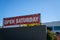 Open Saturday sign hanging on top of store building on sunny day