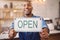 Open, sign and closeup of man in shop, store and advertising notice of retail shopping time, board or trading