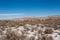 Open snow covered desert with bushes and cactus with mountain range with clear blue sky