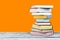 Open stacking book, hardback colorful books on wooden table and orange background. Back to school. Copy space for text. Education