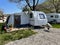 An open tent in front of a travel trailer at a caravan campsite. Caravan camping concept.