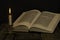 Open Torah and a burning candle in a candlestick on a wooden surface on a dark background