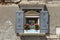 Open window with mosaic of virgen mary with flower pot and historic iron shutter