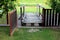 Open wooden backyard fence doors leading towards small wooden boards and logs bridge over narrow water canal surrounded with grass