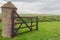 Open wooden gate into farmers green field.  Old stone pillar.