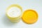 Open yellow cream jar with white lotion on white background.