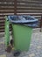 Opened green dumpster on brown wooden fence background.