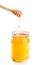 Opened honey jar on white background with wooden honey dipper on top and drop honey