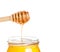 Opened honey jar on white background with wooden honey dipper on top pouring honey
