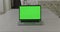 The opened laptop with green screen is in front of camera on table