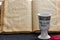 An opened old Jewish Bible, porcelain kiddush wine cup and red jewish bale on black background. Selective focus