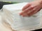 Opened pack of white paper napkins and females hand touching napkins, close up view. Stack of paper towels on table