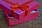 Opened pink gift box with red ribbon and golden stitching on the wooden background as a symbol of giving and getting gifts