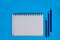 An opened white paper diary beside three wood pencil crayons over a blue background