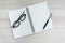 Opening white blank paper note book with pen on the right and glasses on the left on light grey wooden table background with copy