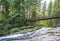 Openwork foot bridge over a small mountain river with boulders overgrown with bright green moss in a wild forest