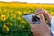 The operator holds the remote control of the drone in his hands against the background of a sunflower field and clouds. A farmer