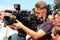 Operator with professional television camera shoots video at rally, protest, event. Journalist correspondent takes interview, live