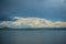 The opposite shore of the azure lake against the blue sky with white clouds.