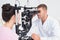 Optician examining female patients eyes through slit lamp