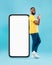 Optimistic black man showing ok gesture, leaning on big smarthone with blank screen, recommending new mobile app, mockup