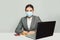 Optimistic businesswoman in protective medical mask using laptop working in office