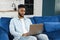 Optimistic confident dark-haired handsome guy using laptop for work. Multiracial freelancer man sitting at the sofa and