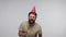 Optimistic delighted bearded guy with funny cone hat laughing and blowing party horn, celebrating birthday