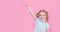 Optimistic, smiling happy little girl taking off the medical mask from face on a pink background with hand up showing end of the