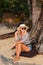 Optimistic woman in a stylish hat and glasses smiles, sitting at his oceanfront Resort, on a summer day