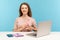 Optimistic young woman, volunteer or manager, sitting at workplace with laptop and holding pink ribbon