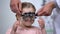 Optometrist putting special glasses on little girl, diagnosing Lazy eye illness