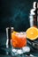 Orange Alcohol cocktail with red vermouth, bitter, soda, orange zest and ice, dark wooden bar counter background, bar tools,