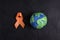 Orange awareness ribbon and planet Earth symbol on a black background