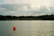 Orange ball buoy floating on a quiet lake beside a park