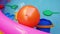 Orange ball and toys for playing in colorful rainbow inflatable swimming pool in clear blue water. Summer active lifestyle