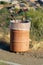 Orange barrel trash can with white translucent bag with natural foliage and shrub background with suburban homes