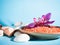 Orange bath salt in a saucer with shells and flower on a blue background with a shadow from a tropical plant. Copyspace