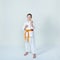 With an orange belt girl stands in the rack karate