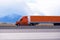 Orange big rig semi truck with long semi trailer running on the