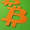 Orange bitcoin sign close-up on green background square photo in the style of minimalism