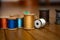 Orange, Blue, Light Blue, Gold, Yellow, White, Black, and Silver Threads on Wooden Spools On a Series of Wooden Planks