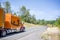 Orange bright big rig semi truck with long cab for comfort rest of truck driver transporting goods in dry van semi trailer running