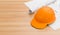 Orange or brown safety helmet on wooden table with blueprints. Safety helmet for welders and workers with high heat application.