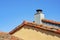 Orange building exterior with adobe red roof tiles and white stone chimney with metal vent and clear blue sky background